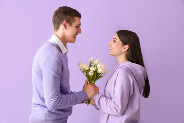 Happy young couple with tulips on lilac background