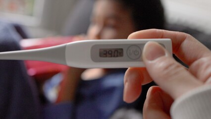 Close-up view of a thermometer showing a high temperature against a blurry background of a child