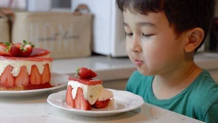 Cute little boy eating with pleasure a fresh strawberry cake 