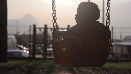 Silhouette of baby swinging on a swing towards the sun