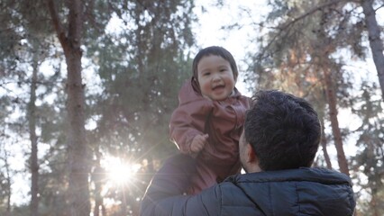 Father tosses the baby up in front of the trees. View from below