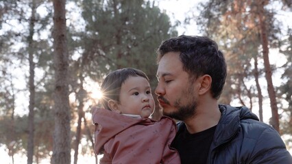 A loving father holding a baby in his arms and and kissing him tenderly in nature