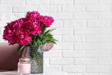 Vase of red peonies with candle on coffee table and couch near white brick wall