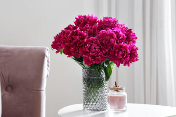 Vase of red peonies with candle on coffee table in living room