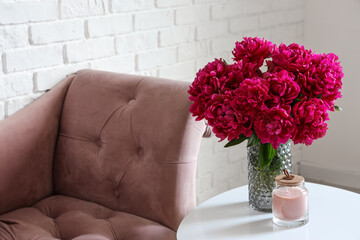 Vase of red peonies with candle on coffee table and couch near white brick wall © Pixel-Shot