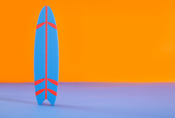 Mini surfboard on blue table against orange background