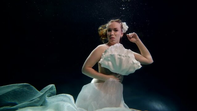 sexy topless woman floating underwater, covering her breasts by white fabric flower, fabulous fairy