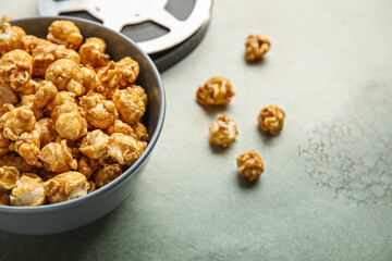 Bowl with tasty popcorn and film reel on grey background