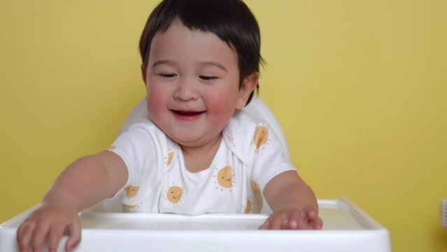 Cute asian baby sits on highchair on yellow background