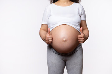 Close-up pregnant woman with naked belly, thumbs up, showing approval hands sign, expressing...