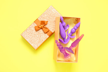 Gift box with different dildos on yellow background