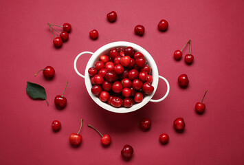 Colander with sweet cherries on red background