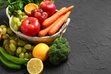 Wicker basket with different fresh fruits and vegetables on black background