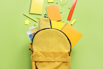 Yellow school backpack with notebooks, pencil case and watercolors on green background