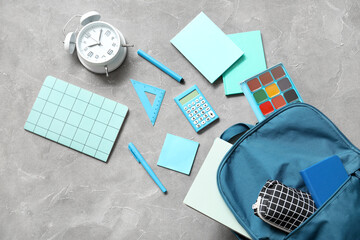 Blue school backpack with alarm clock, notebooks and watercolor on grey grunge background