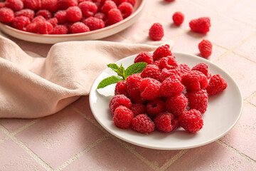 Plates with fresh raspberries on pink tile background