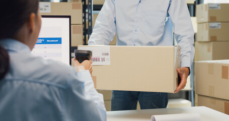Close-up Asia business partner man hold cardboard box and girl partner wear formal shirt sit front computer use barcode machine scanner stock online data at warehouse. Startup small business concept.