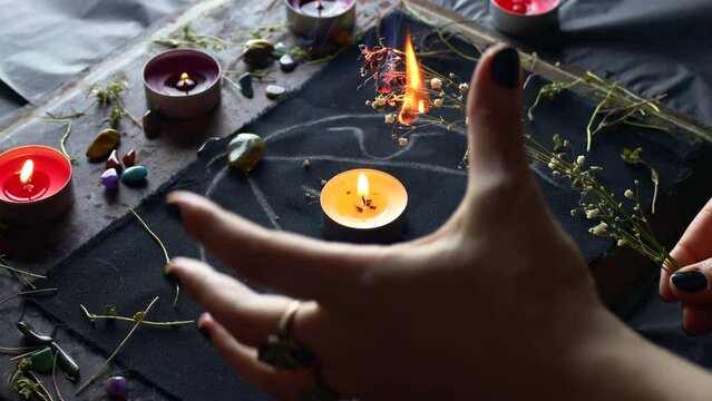 Witch hands burning herbs for a black magic ritual with the help of magical altar, candles and crystals. Sorcerer rite of witchcraft and occultism. Halloween occult, esoteric and divination concept.