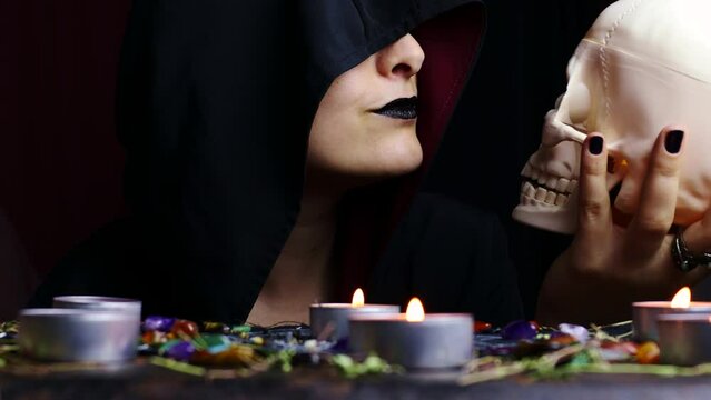 Witch hands holding and kissing a scary skull for a black magic ritual on a magical altar. Sorcerer rite of witchcraft and occultism. Halloween occult, esoteric and divination concept.
