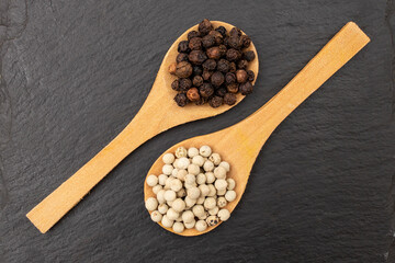 Black vs white pepper seeds in two wooden spoons