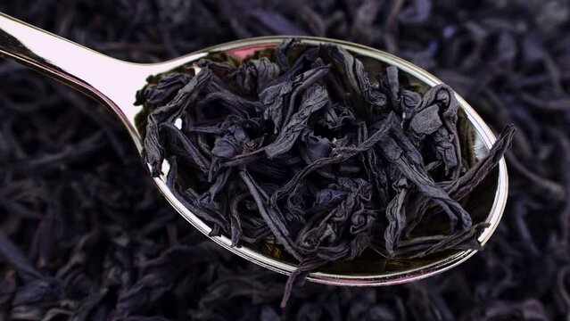 Dried black ted leaves in the spoon with circle rotation close up