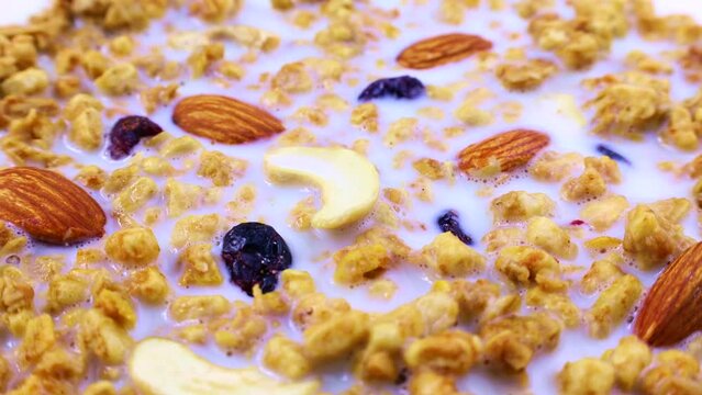 Healthy yellow organic granola breakfast flakes with almonds, cashew nuts and cranberries with milk circle rotation close up
