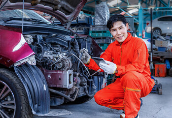 Asian mechanic in orange uniform looking at tablet about car engine while repairing in garage