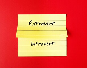 Yellow note stick on red background with handwritten text - INTROVERT EXTROVERT, different traits personalities - Introverts tend to feel drained after socializing while extroverts feel energized