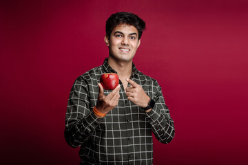 Young Man With Red Apple. Recommends and Promotes Delicious Apple Brand Isolated On A Red Studio...