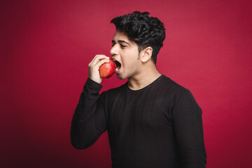 Healthy diet concept, young man biting red organic gala or fiji newzealand apple isolated on a red...
