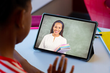 Diverse schoolboy with happy female teacher having class during tablet video call