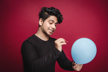 Young Man's Skillful Aim to Pop Balloon with Toothpick isolated on a red studio background.