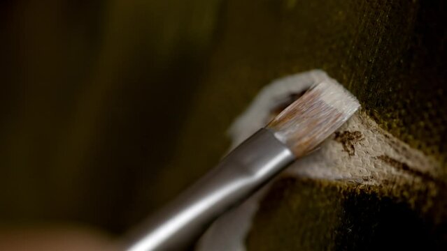 Detailed closeup of wide fine tip paintbrush spreading white paint on canvas