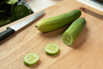 Fresh picked cucumber slices prepare for cooking on wooden bamboo chopping board next to sharp knife in the kitchen table at home while cooking