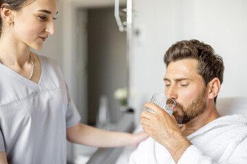 Adult patient drinking water while resting in medical ward. Medical support and assistance during the rehabilitation in clinic