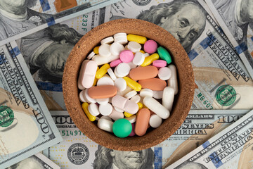 Colorful pills and capsules in a bowl on the background of dollars. The concept of expensive medicine.