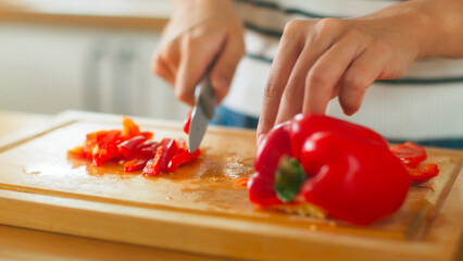 Close up of happy attractive young Asian woman hand slicing red bell pepper on wooden cutting board preparing vegetable enjoy cooking healthy vegetarian food dinner for husband and family