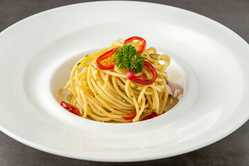 Spaghetti with paprika on white porcelain plate on dark stone table