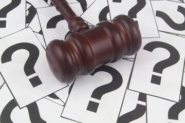 Legal FAQ concept. Wooden judge gavel on question marks background.