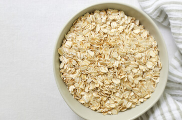 Raw oatmeal in a gray bowl on a white tablecloth with a kitchen napkin. Concept of healthy breakfast. Vegetarian and vegan. Horizontal orientation. Selective focus. Copy space. Top view
