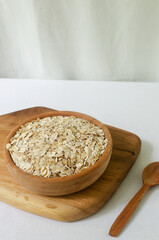 Raw oatmeal in a wooden bowl on a cutting board with a teaspoon. Concept of healthy eating. Vegetarian and vegan food. Rustic style. Vertical orientation. Selective focus.
