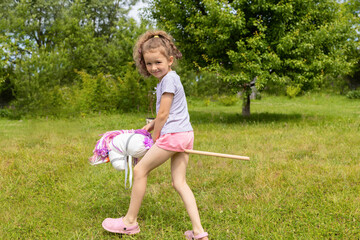 beautiful little girl cowboy playing running riding on toy stick horse in park in nature on summer....