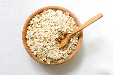 Raw oatmeal on a wooden bowl with a teaspoon on a white background. Concept of healthy eating....