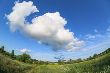 Beautiful fluffy clouds in the blue sky above the hill