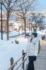 Fototapeta na wymiar Woman tourist Visiting in Hakodate, Traveler in Sweater sightseeing Hachiman Zaka Slope with Snow in winter. landmark and popular for attractions in Hokkaido, Japan. Travel and Vacation concept