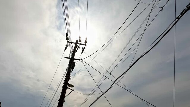 Broken electricity wires swaying slow motion in wind with bright sun in background