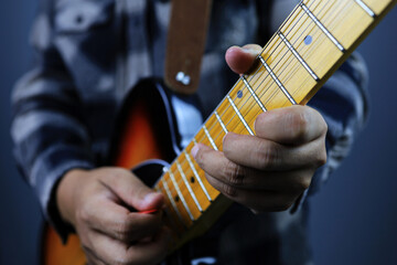Left hand close up of guitarist with red pick standing and playing electric guitar sunburst solid...