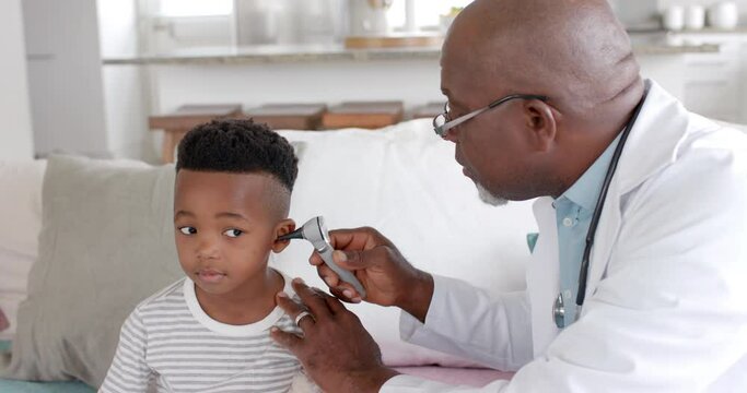 Senior african american male doctor checking ear of boy patient with otoscope, slow motion