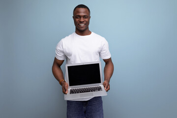 successful young african man in white t-shirt working remotely using laptop on studio background...