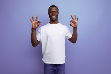 positive friendly young african man in white t-shirt on studio background with copy space